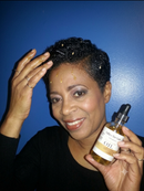 Hair A Do Growth Oil by Cathy’s New Look; amber glass dropper bottle held by a smiling woman with short black curls